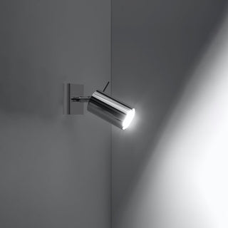 Chrome adjustable wall spotlight switched on, casting a bright beam of light onto the adjacent dark wall surface.
