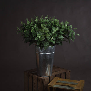 Artificial eucalyptus in a galvanised bucket, resting on dark wooden crates against a brown background.