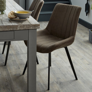 Coffee faux leather dining chair pulled up to a wooden dining table set with a bowl of soup.