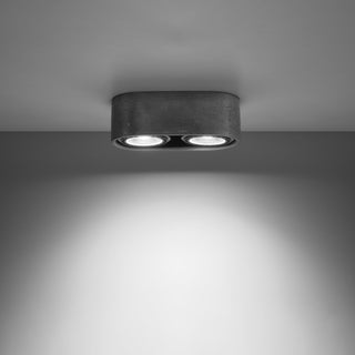 Concrete ceiling light fitting with two illuminated spotlights casting a bright beam onto the wall below.