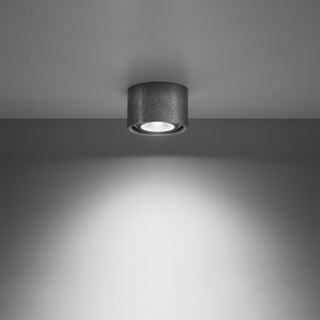 Concrete ceiling lamp switched on, projecting a bright circular beam onto the wall.