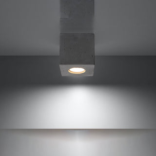 Concrete ceiling light fixture illuminated, casting a warm spotlight beam onto a wall below.