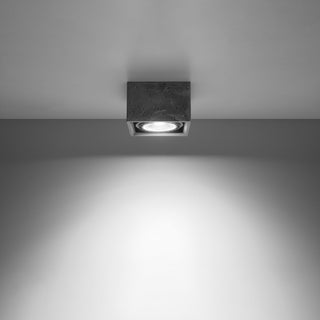 Square concrete ceiling lamp switched on, casting a bright spotlight beam onto the wall below.
