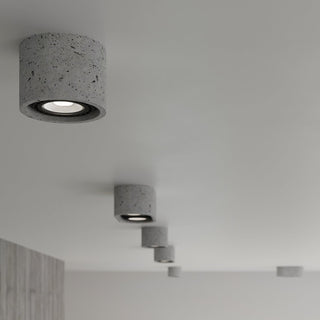 Perspective view of multiple cylindrical concrete spotlights installed in a line on a white ceiling.
