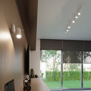 White cylindrical wall lamp installed in a modern living space, casting a warm beam onto a wooden feature wall.