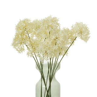 Artificial cream allium stems displayed in a translucent, hourglass-shaped glass vase.