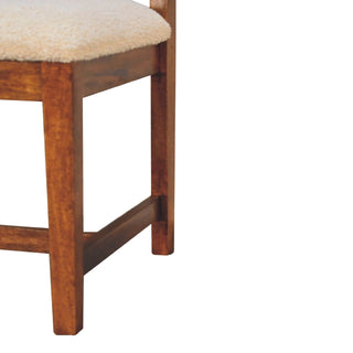 Detail view of the dark wooden front legs and side rail joint below the cream boucle seat.