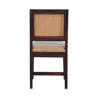 Straight-on view of the dark wooden chair with woven rattan back and thick cream boucle upholstery.
