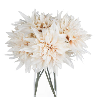 Several artificial cream dahlia stems grouped together in a transparent vase.