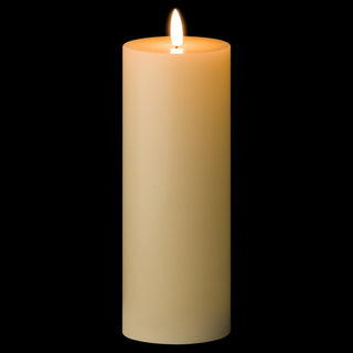 Tall cream LED pillar candle glowing brightly in the dark against a black background.