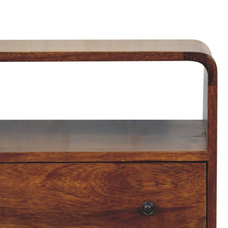 Detail shot showing the curved top edge, open shelf, rich wood grain texture, and dark metal drawer handle.