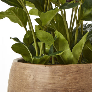 Close-up showing the earthy texture of the taupe pot and the artificial green leaves emerging from the soil.