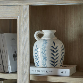 Close detail of light wood grain on the dresser top frame and shelf, styled with books and a jug.