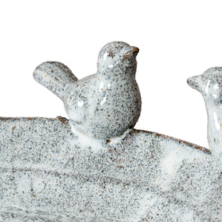 Extreme close-up of one speckled ceramic bird figure sitting on the rim of the bath, showing its tail and beak.