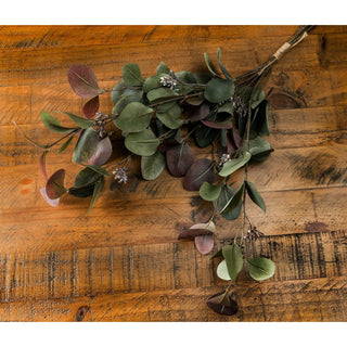 Detail shot of artificial eucalyptus foliage and tiny white buds resting on distressed wood.