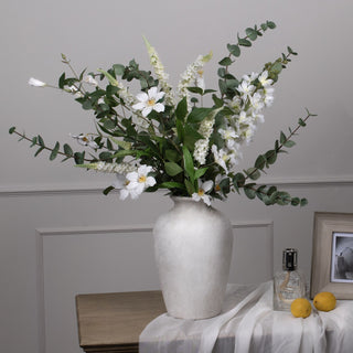 Faux eucalyptus foliage in a large mixed white floral arrangement on a side table.