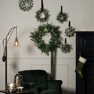 Large frosted eucalyptus wreath hanging on a wall display with smaller wreaths, above a green armchair.