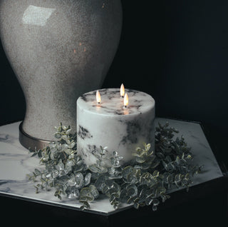 Frosted eucalyptus wreath surrounding a large LED candle on a marble side table in a dark setting.