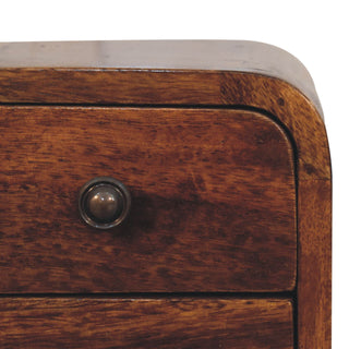 Close detail of the curved chestnut cabinet corner and round bronze drawer knob.