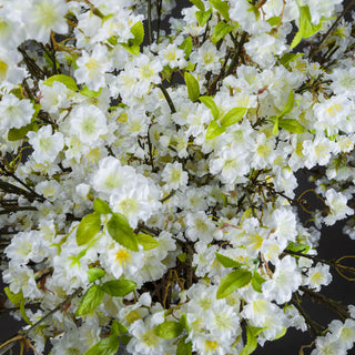Close-up detail of dense clusters of white faux cherry blossoms, bright green leaves, and dark brown stems.
