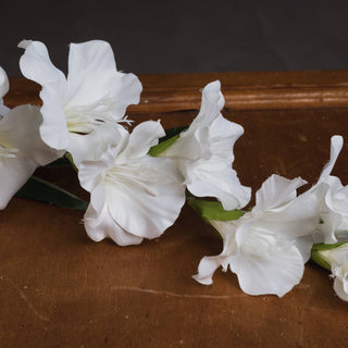 Close-up detail of three open white faux gladioli flowers resting on a dark wooden surface.