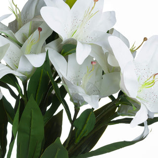 Close up detail of clustered faux white lily heads, showing speckled petals, pink stamens, and dark green leaves.