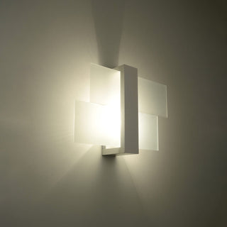 Warm light glowing through the four layered frosted glass panels of the white wall lamp against a neutral wall.