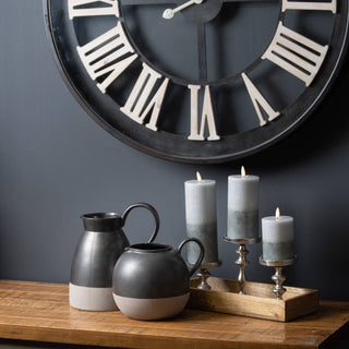 Three lit two-tone ombre LED candles on silver holders, styled on a wooden surface below a large clock.