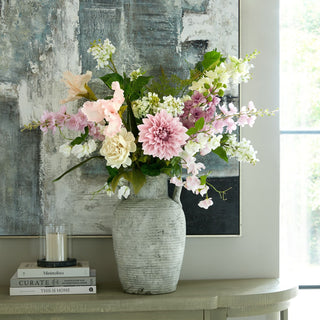 The pale apricot iris integrated into a large artificial floral display in a textured vase on a wooden table.