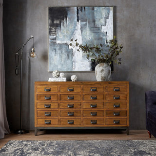Pair of white distressed artichoke sculptures styled on a large wooden multi-drawer cabinet beneath abstract wall art.