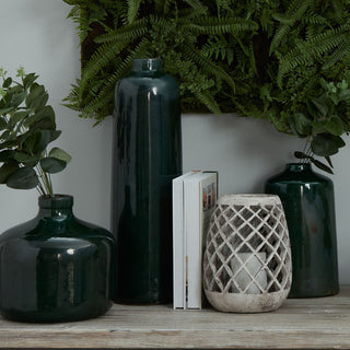 Grouping of three emerald green glazed vases of different shapes on a wooden surface, styled with books and a lantern.
