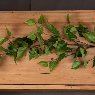 Close-up of green artificial branch leaves and brown stems lying flat on a rustic wooden surface.