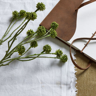 Close-up of the textured green floral heads and stems of the artificial Craspedia on white fabric.