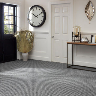 Dried palm arrangement in a large vase on a grey carpeted hallway floor, next to a black glazed door.