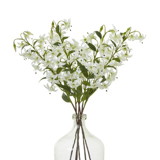 Artificial white lily sprays densely arranged in the neck of a clear glass bottle.
