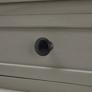 Close-up of the matte black round knob on the grey wooden drawer front.