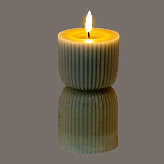 Lit grey carved LED candle with vertical fluting, reflected on a shiny surface below.