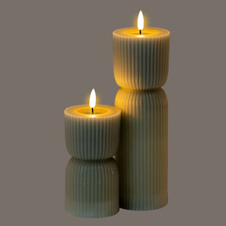 Pair of grey carved LED candles glowing warmly in the dark, highlighting the vertical ribbed texture.