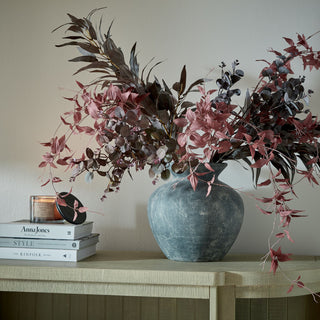 Styled scene showing the Amalfi vase filled with dark red branches, next to books and a burning candle.