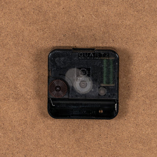 Detail of the black quartz movement mechanism on the clock's brown fibreboard rear.