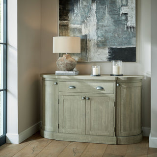 Two glass lantern candle holders displayed on a wooden sideboard next to a lamp and abstract artwork.