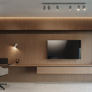Grey wall lamp fixture mounted on a wood-panelled wall above a desk area, switched on and illuminating a laptop.