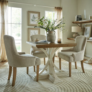 Artificial gypsophila mixed with other faux flowers in a vase on a square wooden dining table in a styled room.