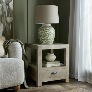 Washed oak side table with lamp and books, next to a sofa in a styled living room scene.