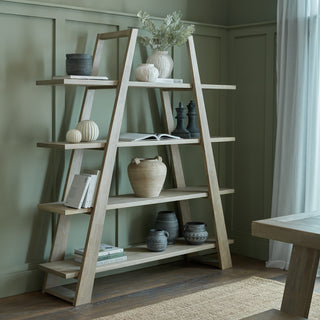 Light wood four-shelf apex unit styled with ceramics and books, set against a sage green panelled wall.