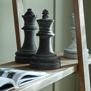 Close-up detail of a light wood shelf showing the grain, styled with large black chess pieces and an open book.