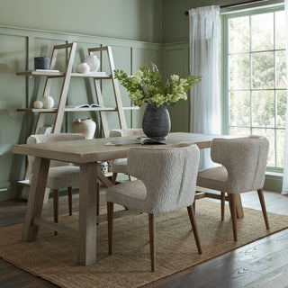 Large light wood dining table set with four upholstered chairs in a sage green room.