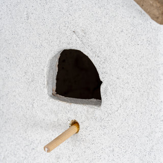 Close detail of the arched entrance hole and wooden perch on the rough white textured surface of the birdhouse.