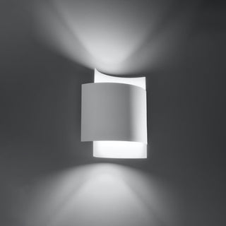 Curved white layered wall lamp illuminated against a dark grey background