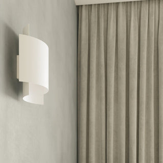 White layered wall lamp mounted on a textured grey wall beside pleated taupe curtains.